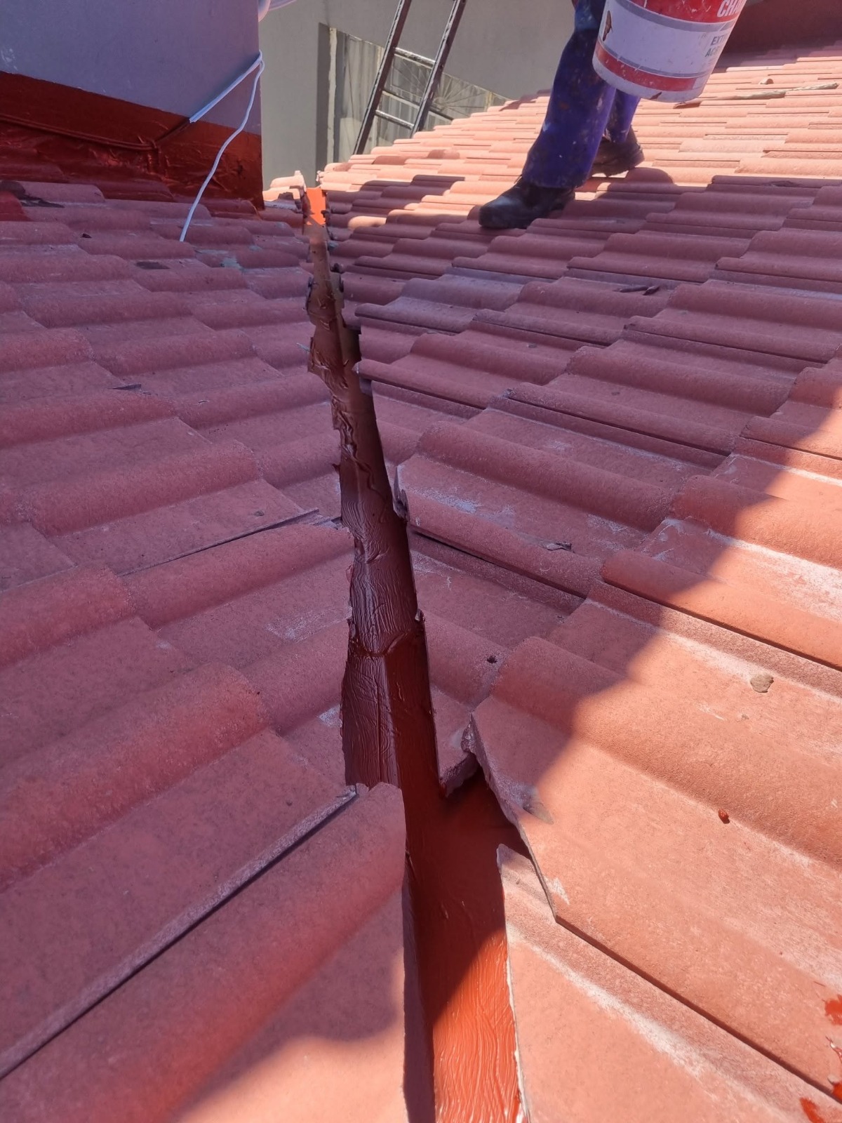 Close-up of roof valley waterproofing with liquid rubber sealant applied between roof tiles