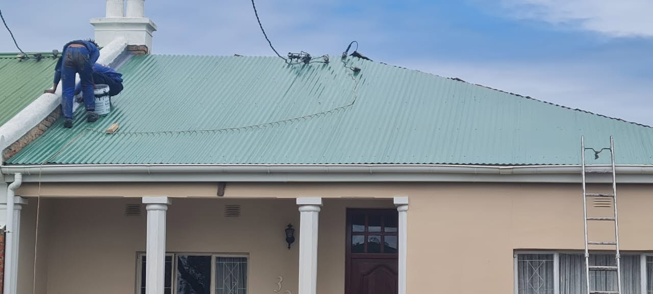 Worker applying roof coating on corrugated metal roof with liquid rubber product