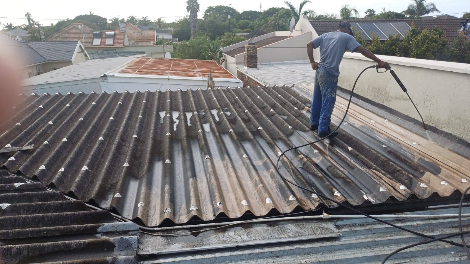 Worker cleaning roof surface with pressure washer before waterproofing